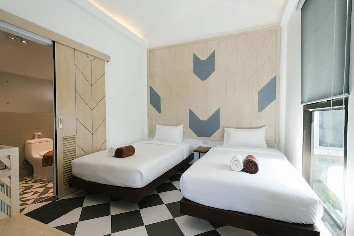 Habitación de hotel con dos camas, piso a cuadros, una puerta corredera y una pared con diseños geométricos.