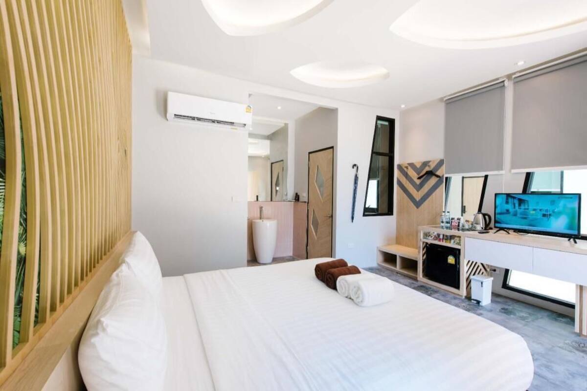 Habitación de hotel moderna con una cama grande, televisión, escritorio con computadora y un baño visible al fondo.
