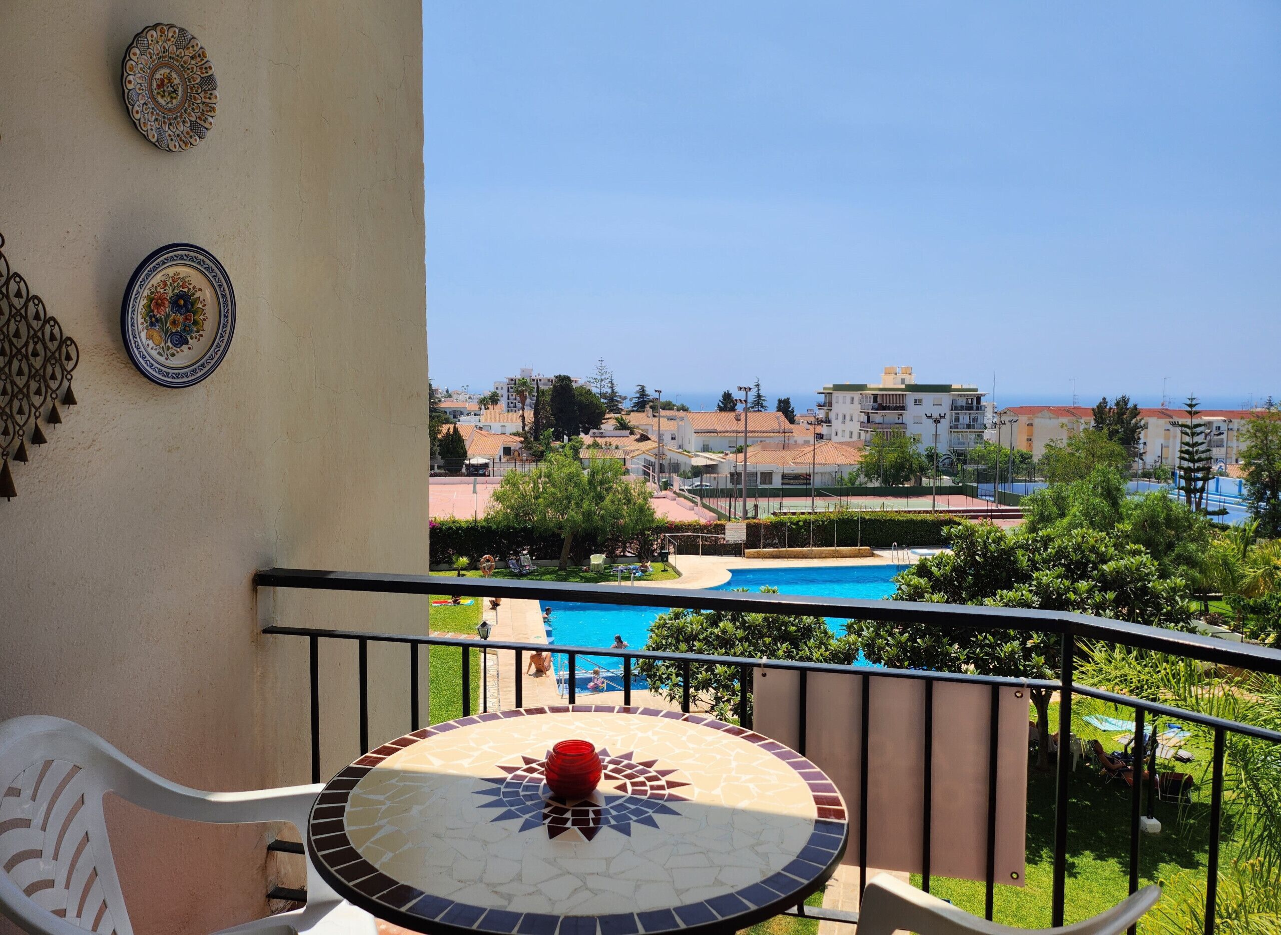 A balcony with a view of a swimming pool, a tiled table, and decorative plates.