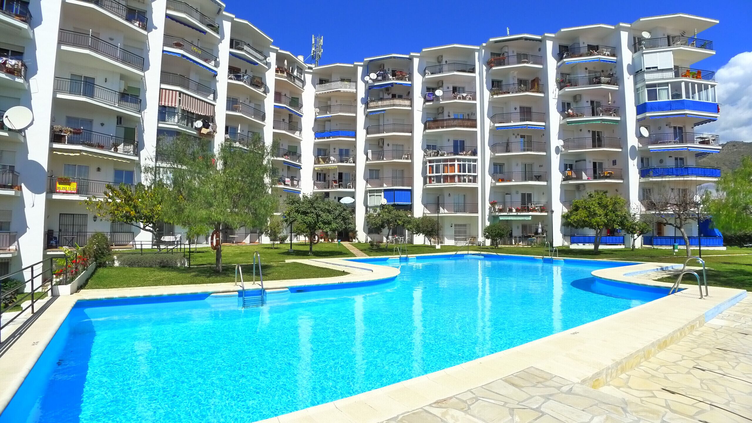 A multi-story hotel with a central swimming pool, balconies, and a clear sky.
