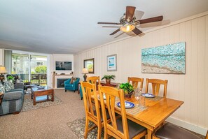 A living room with a fireplace, a dining table set for four, and a ceiling fan.