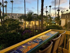 A balcony with a mosaic table, surrounded by palm trees and a view of a resort building.