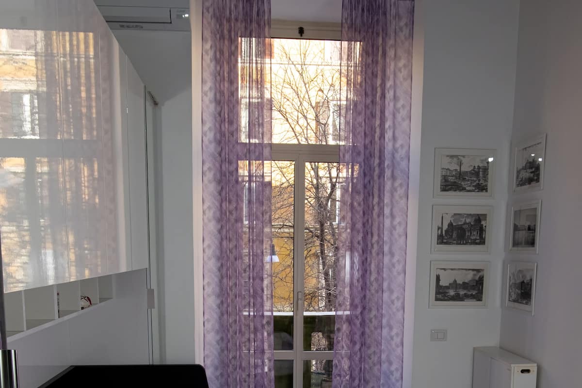 A modern bedroom with a large bed, purple bedding, and a window with purple curtains.
