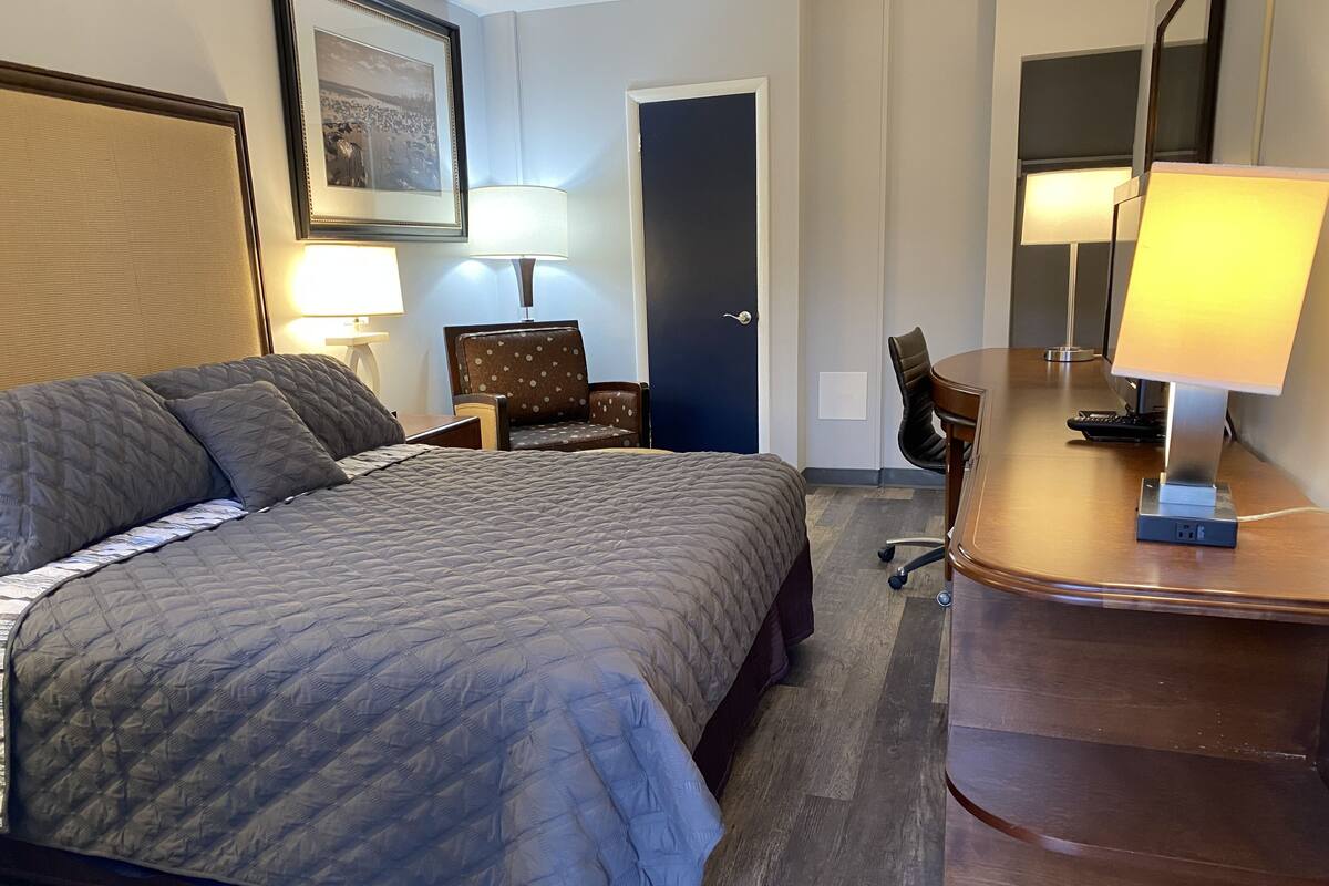 Une chambre d’hôtel avec un grand lit, un bureau avec une lampe, une chaise et un tableau encadré au mur.