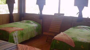 A room with two single beds, a wooden chair, and a window with curtains.
