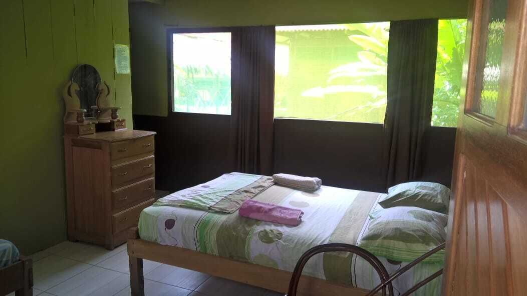 A bedroom with a bed, a wooden dresser, and a window with curtains.