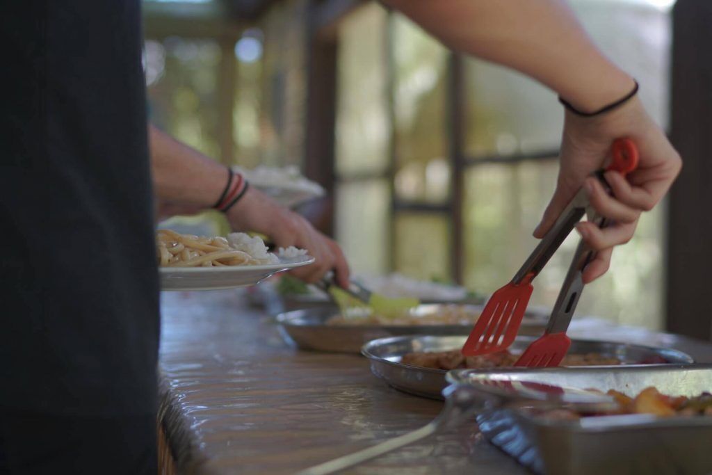 Una persona sirviendo comida en una mesa de buffet con diferentes platos y utensilios.