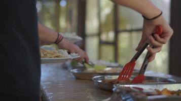Una persona sirviendo comida en una mesa de buffet con diferentes platos y utensilios.