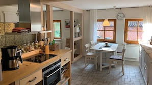 Cozinha moderna com armários de madeira, forno embutido e espaço de jantar com mesa e cadeiras.