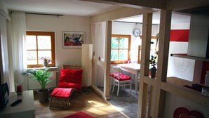 Um quarto acolhedor com piso de madeira, uma cadeira vermelha, uma mesa pequena e uma janela com cortinas.