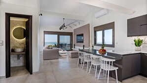 Una cocina moderna con una isla central, taburetes blancos de bar y un ventanal con vistas al mar.