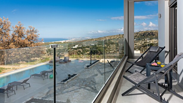 Un balcón con barandilla de vidrio que da a una piscina y una vista panorámica de un paisaje montañoso.