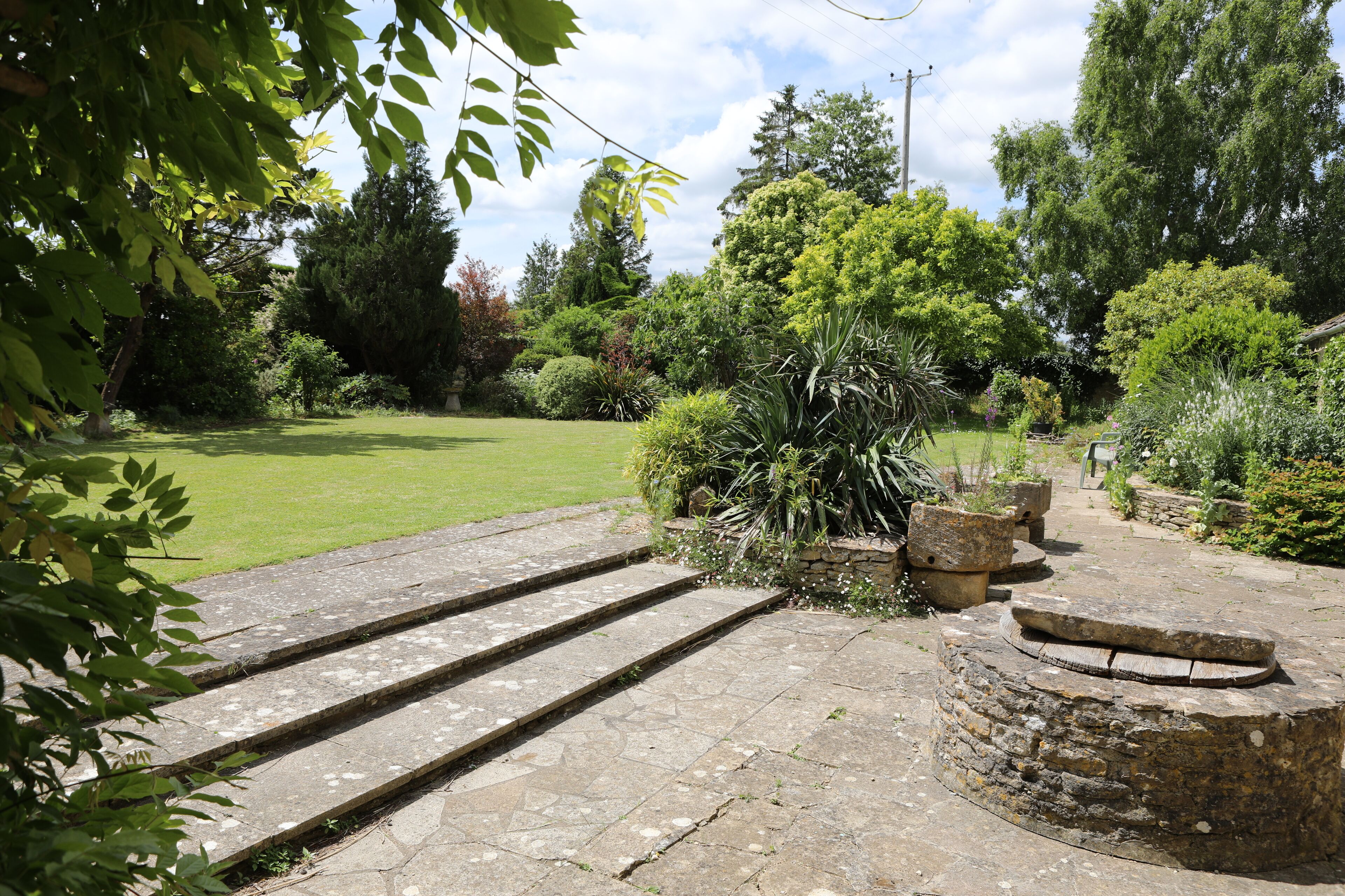 A garden with stone steps leading to a stone wall, surrounded by lush greenery and trees.