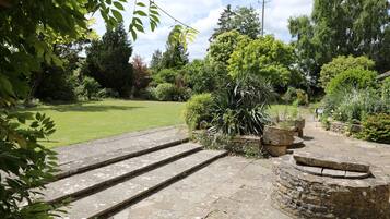 A garden with stone steps leading to a stone wall, surrounded by lush greenery and trees.
