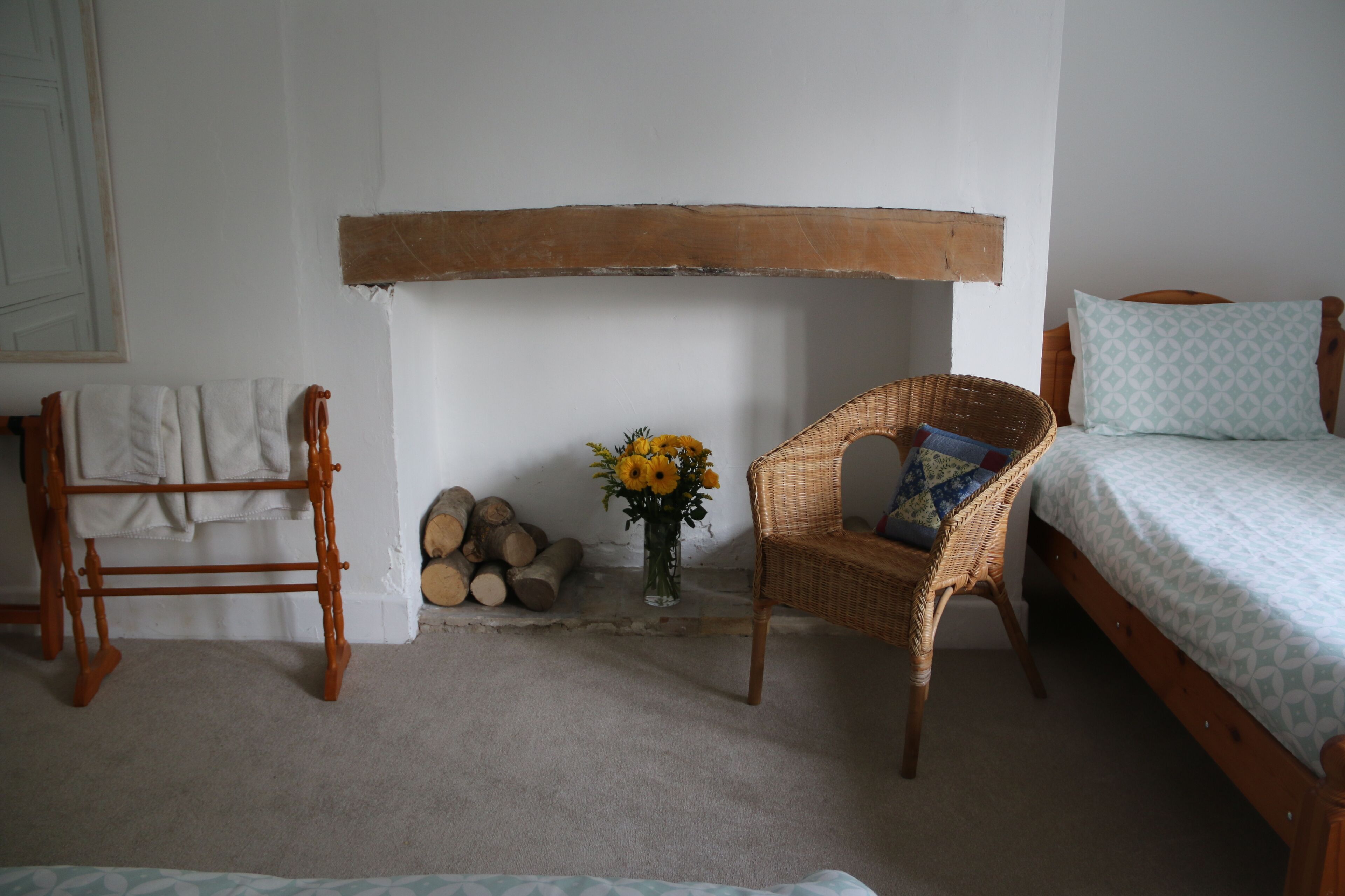 A bedroom with a bed, a chair, a wooden bench, a vase with flowers, and a stack of firewood.
