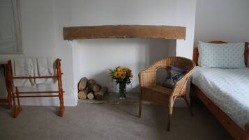 A bedroom with a bed, a chair, a wooden bench, a vase with flowers, and a stack of firewood.