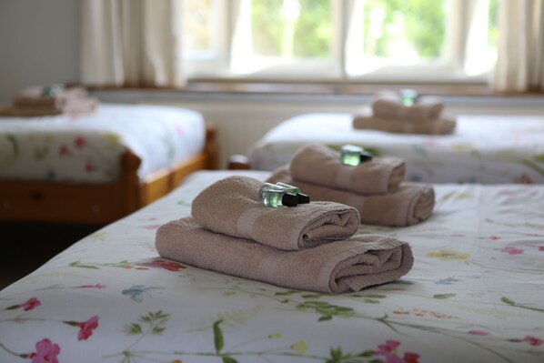A hotel room with two beds, each with a floral bedspread and towels. - Beautiful Cotswolds farm house with period features and a beautiful garden. (Clanfield)
