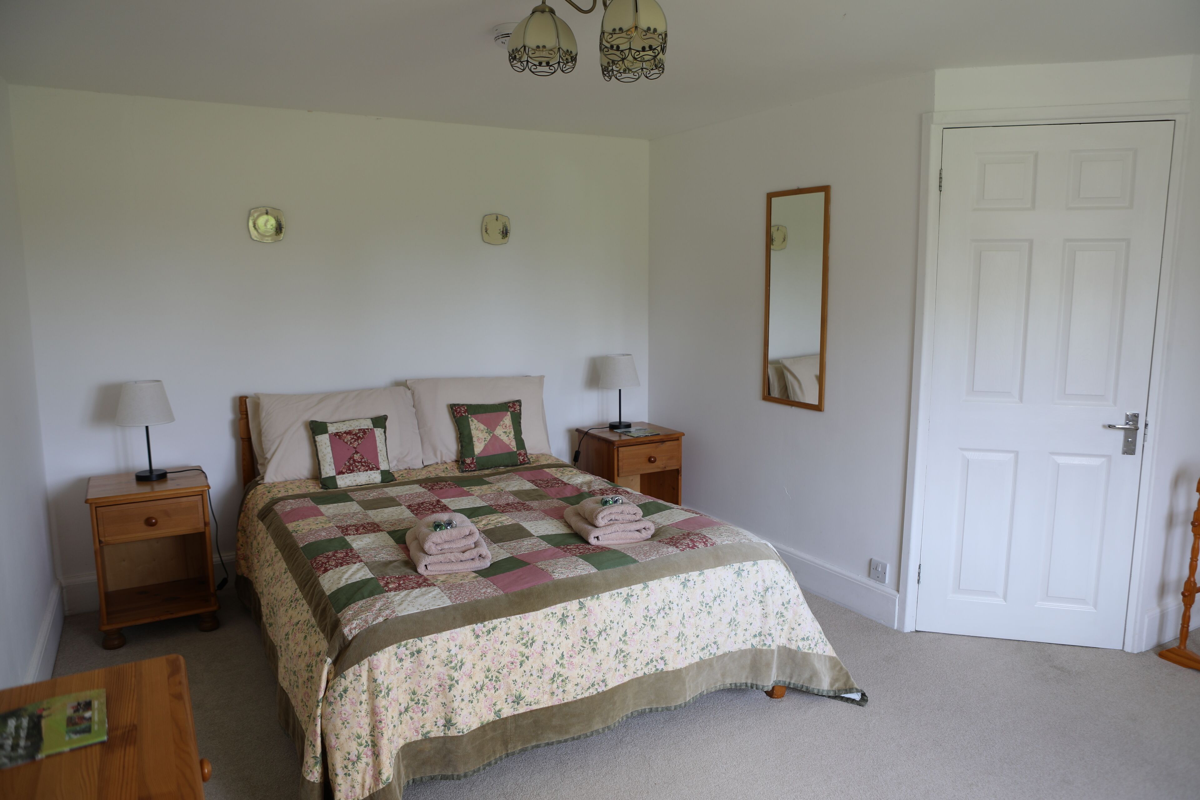 A bedroom with a bed, two bedside tables, a nightstand, a dresser, a mirror, and a door.