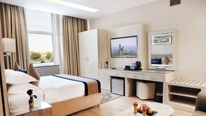 Habitación de hotel con cama, escritorio, silla, una mesita con bebidas, televisión y vista a la ciudad.