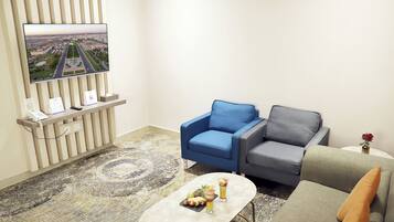 A modern living room with a flat-screen TV mounted on a wall, two sofas, a coffee table with fruit and drinks, and a patterned carpet.