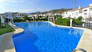 A swimming pool with clear blue water, surrounded by white buildings with red-tiled roofs, and a mountainous backdrop. - Sleeps 9 | Casa Vista Bella | CG R1248 (Nerja)