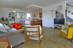 A spacious living area with a sofa, a rocking chair, a yellow armchair, a dining table, and a television.