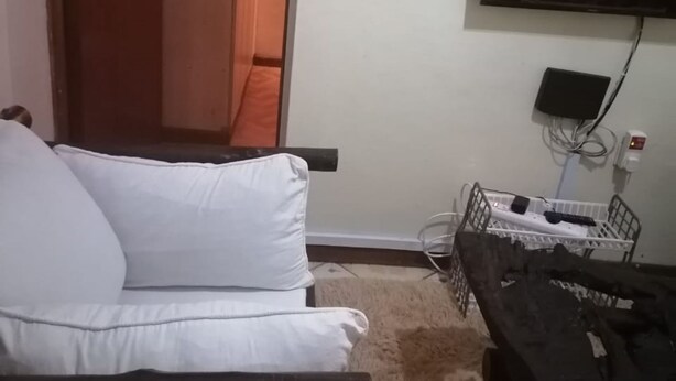 Une pièce avec un canapé blanc, un téléviseur fixé au mur et une petite table sur laquelle se trouve une télécommande.