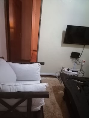A room with a white sofa, a television mounted on the wall, and a small table with a remote control. - Bezalel Apartment (Nairobi)