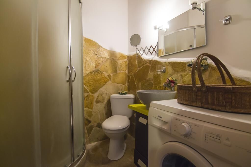 Un baño pequeño con pared de piedra, inodoro, lavabo y lavadora.