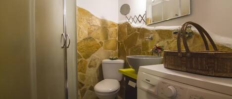 Un baño pequeño con pared de piedra, inodoro, lavabo y lavadora.