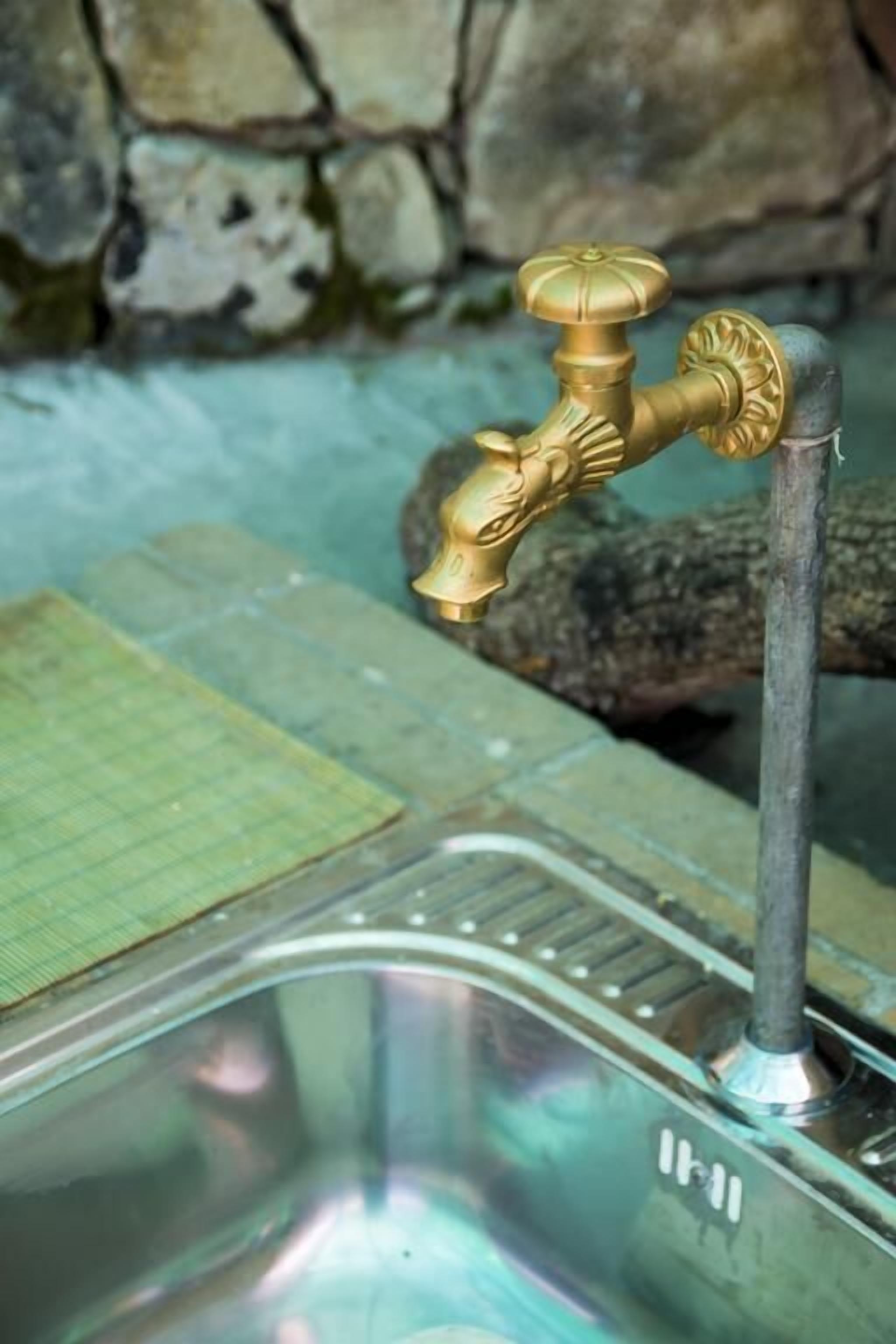 Ein Badezimmer mit goldenem Wasserhahn, einer Steinwand und einer grünen Matte.