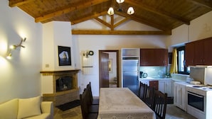 A cozy kitchen with a fireplace, wooden ceiling beams, a dining table, and a stone floor. - Su La Strata house  by CorfuEscapes (Paxos)