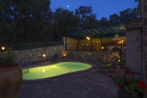 Une piscine avec des chaises longues et un patio couvert équipé d’un barbecue.