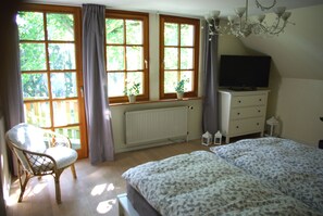 A bedroom with a bed, a chair, a dresser, a television, and large windows with curtains. - Ferienwohnung Sternenhimmel (Bleckede)