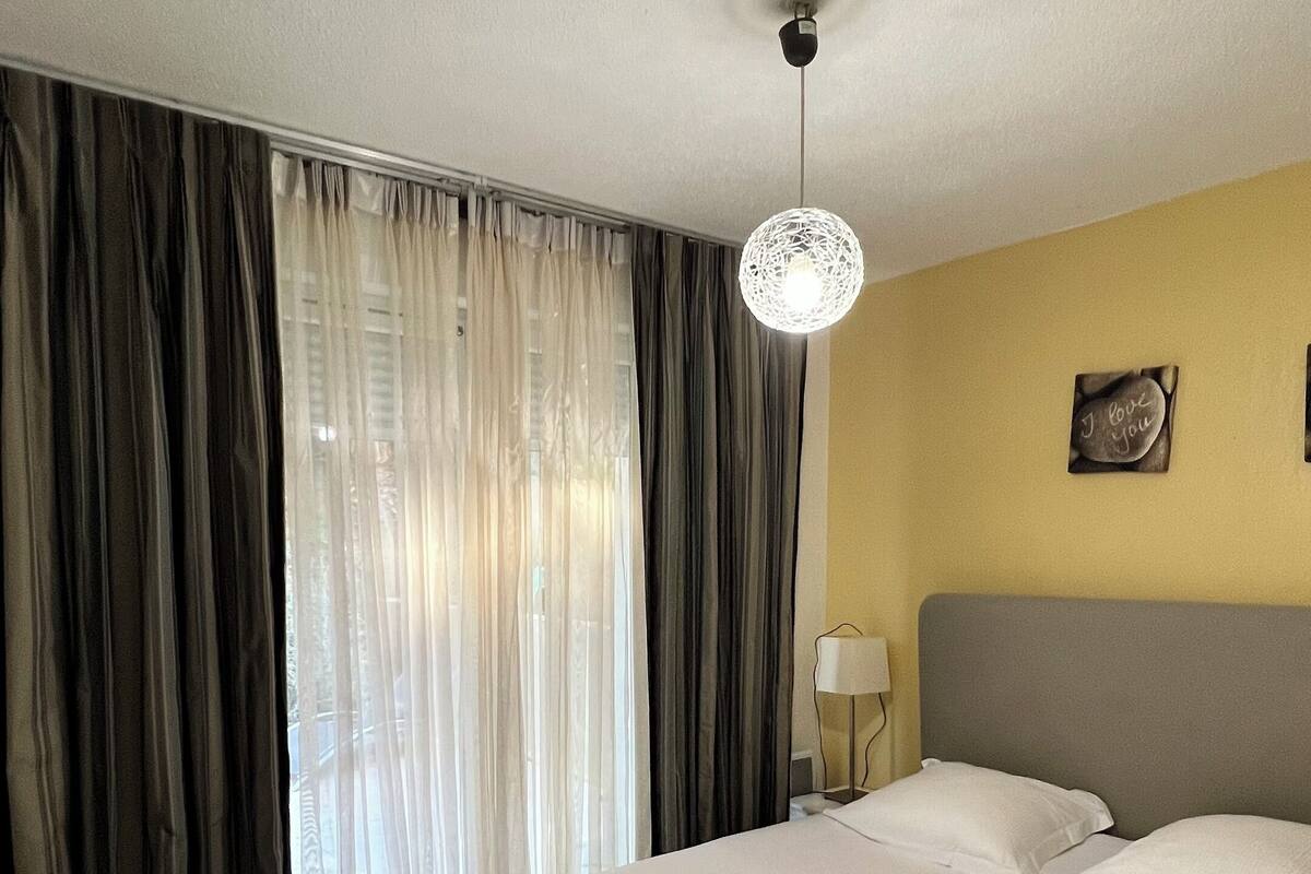 Ein Hotelzimmer mit einem großen Bett, einem Nachttisch, einer Lampe und einem Fenster mit Vorhängen.