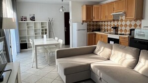 A modern living room with a beige sectional sofa, a white coffee table, and a dining area with a white table and chairs. - Residence les jardins de Natallia (La Seyne-sur-Mer)