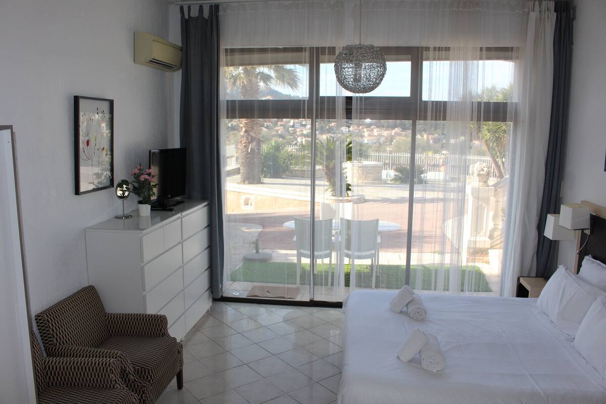 Ein Hotelzimmer mit Bett, einer Sitzecke, einem Fernseher und einem Balkon mit Blick auf die Stadt.