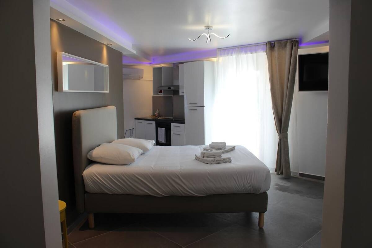 Ein modernes Hotelzimmer mit einem großen Bett, einer kleinen Küchenzeile, einem Flachbildfernseher und einer Deckenleuchte.