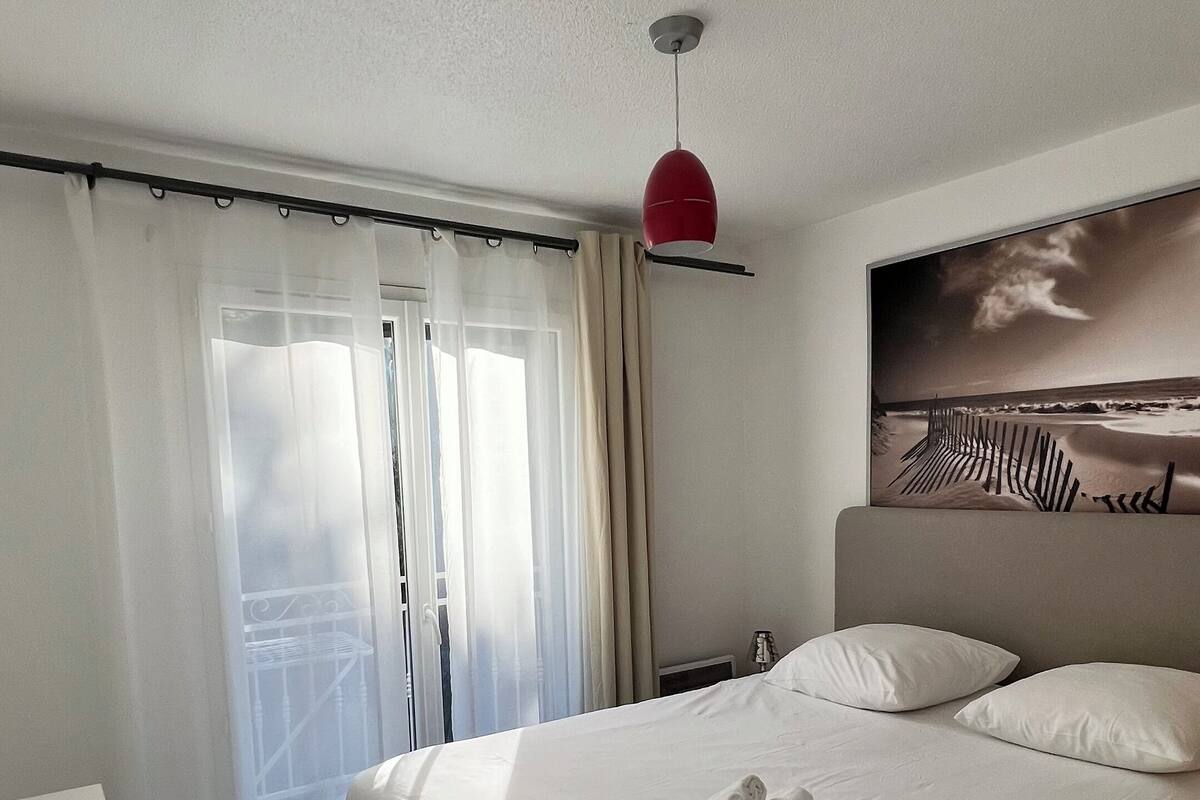Ein Hotelzimmer mit einem großen Bett, einer roten Pendelleuchte, Blick auf den Strand und einer weißen Kommode.