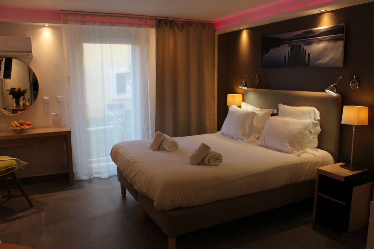 Ein Hotelzimmer mit einem großen Bett, zwei Nachttischlampen, einem Nachttisch, einem Schreibtisch mit Stuhl, einem Spiegel und einem Fenster mit Vorhängen.