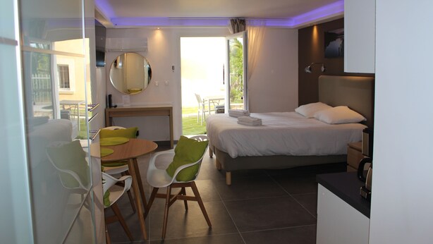 A modern hotel room with a bed, a desk, a chair, and a glass partition. - Residence les jardins de Natallia (La Seyne-sur-Mer)