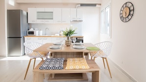 A modern kitchen with white cabinets, a stainless steel refrigerator, and a dining area with a wooden table and two white chairs. - Corfu City Apartments (Corfu)