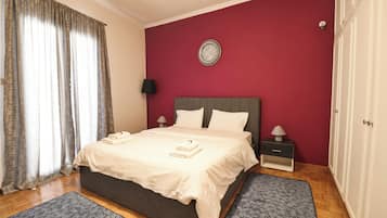 Een slaapkamer met een bed, twee nachtkastjes, een klok aan de muur en een raam met gordijnen.