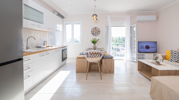 A modern kitchen with white cabinets, a wooden island, and a dining area with a chair and table. - Corfu City Apartments (Corfu)