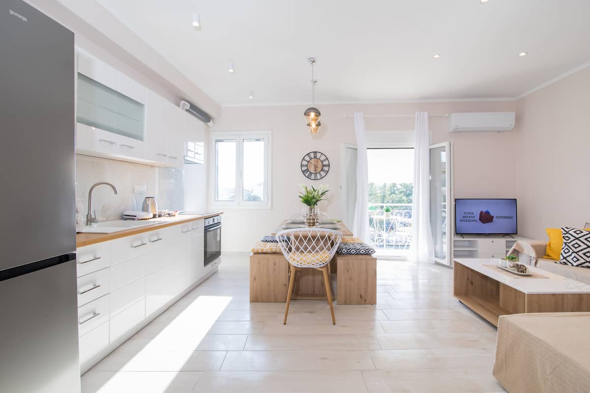 A modern kitchen with white cabinets, a wooden island, and a dining area with a chair and table.