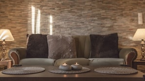 A modern living room with a stone-patterned wall, a leather sofa with dark cushions, and two lit candles on woven placemats. - Corfu City Apartments (Corfu)