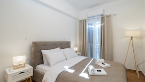 A hotel room with a bed, a bedside table with a lamp, a nightstand with a drawer, and a window with curtains. - Corfu City Apartments (Corfu)