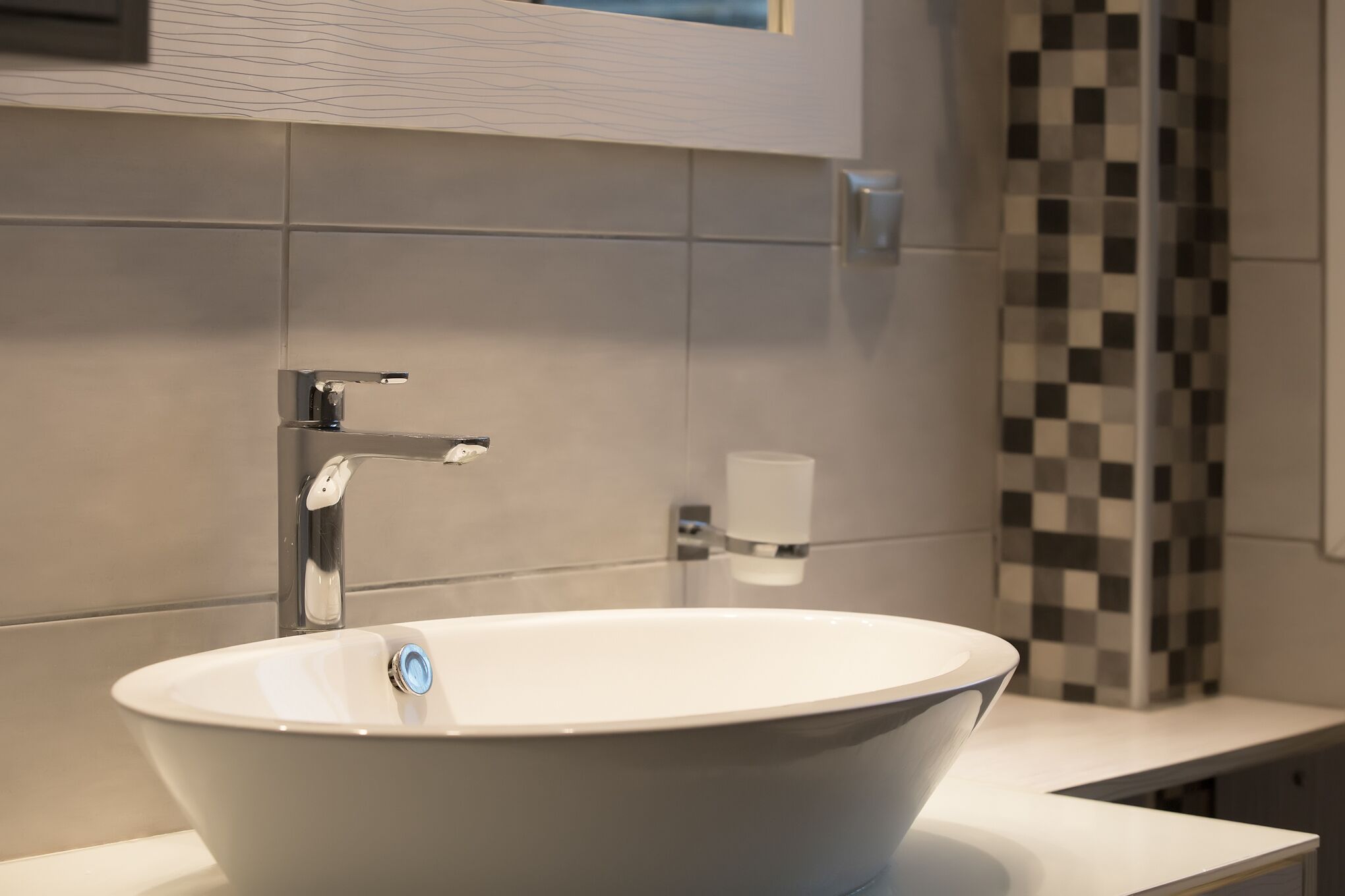 Un bagno moderno con un lavandino bianco di forma ovale, un rubinetto cromato e un dispenser di sapone a parete.