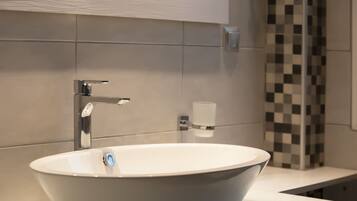 Un bagno moderno con un lavandino bianco di forma ovale, un rubinetto cromato e un dispenser di sapone a parete.