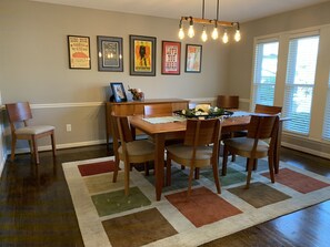 Ein Essbereich mit Holztisch und -stühlen, einem gemusterten Teppich und wandmontierten Leuchten.